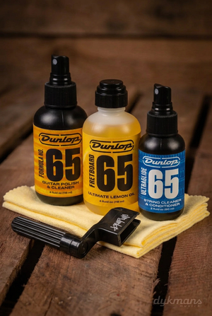 Dunlop 6504 System 65 Guitar Tech Kit met drie flesjes, twee poetsdoeken en snaarwinder op een warme houten achtergrond